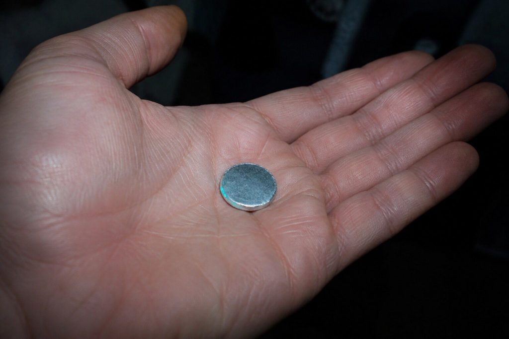 A small metal knockout disc lying in an open palm held under a sink, the cupboard dark behind the hand.