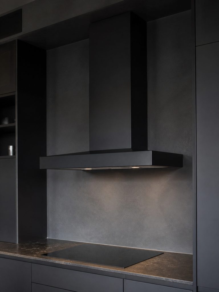 a dark-finish wall canopy in a near-black kitchen — the finish and the palette both