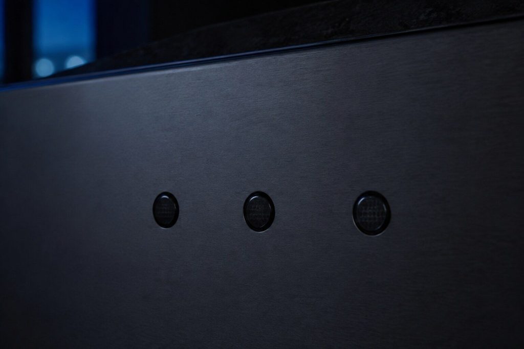 A row of three small unlit indicator lamps on a dark appliance panel, the panel otherwise featureless.