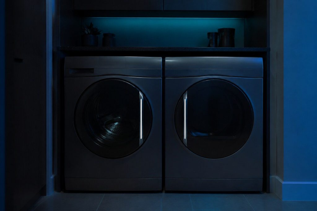 Two appliance doors standing next to each other in a dark run of cabinetry, both closed, their handles catching a single cool highlight along the length.