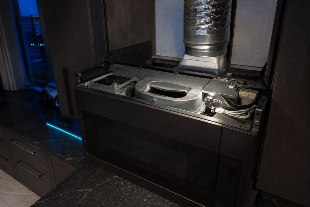 The blower housing inside the top of an over-the-range microwave with its vent flap turned to the other setting, the top cover removed and the ductwork above visible.