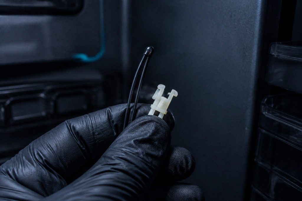 A small bead thermistor on the end of a two-wire lead with its plastic clip, held in a gloved hand against a dark refrigerator interior wall.