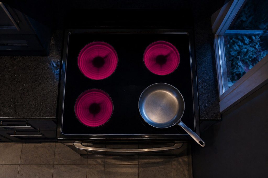 A cooktop seen from directly above in a dark kitchen with three zones showing their indicator glow and the fourth completely dark, an empty pan standing on the dark one.